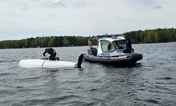 policjant na łodzi policyjnej, a drugi policjant podczas udzielania pomocy sternikowi na przewróconej żaglówce