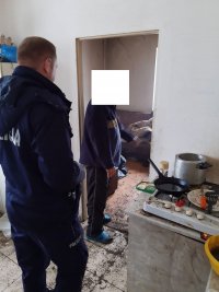na zdjęciu policjant i mężczyzna stoją w brudnym pomieszczeniu