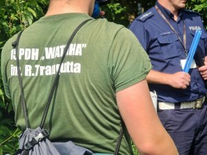 policjant trzyma odblaski, na pierwszym planie mężczyzna w koszulce z nazwą drużyny harcerskiej